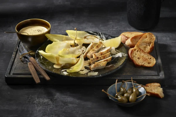 Rezeptbild: Cesars Salad vom Chicorée mit Hühnerbrust. Angerichtet auf einer Platte mit Baguette-Croutons.